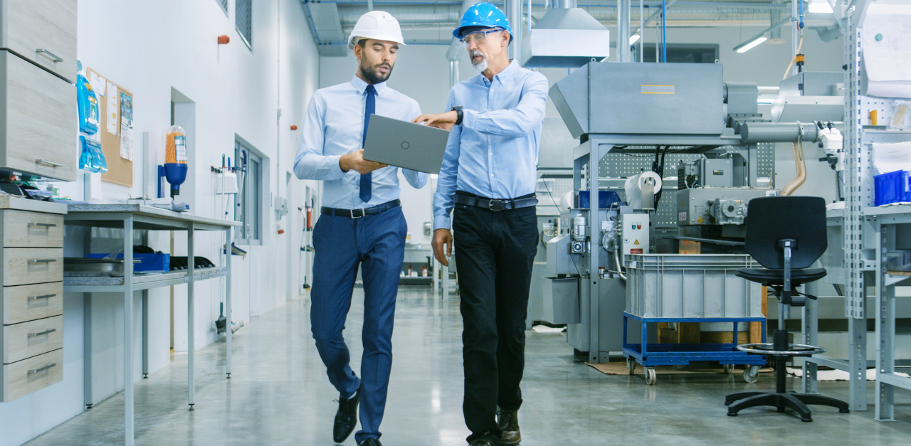 People walking in a factory discussing work on a laptop