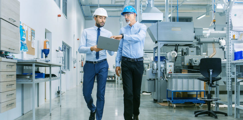 People walking in a factory discussing work on a laptop