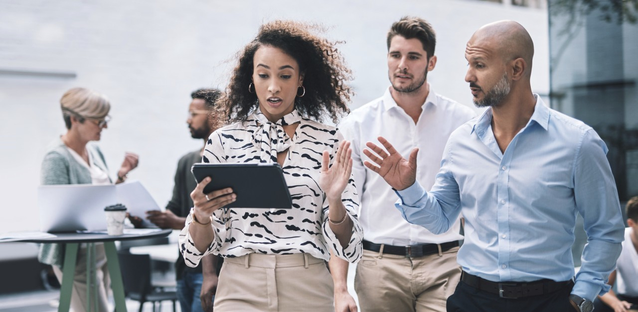 People walking in an office discussing work on a tablet